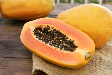 Photo of Tasty cut and whole papaya fruits on wooden table, closeup