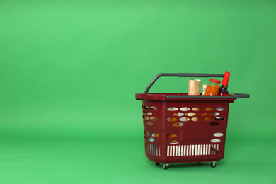 Photo of Shopping basket full of different products on green background. Space for text