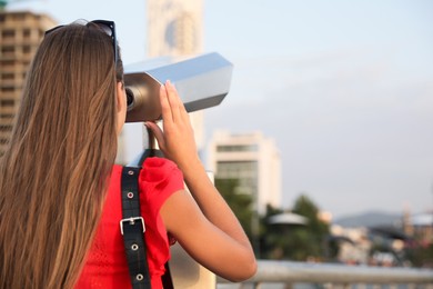 Photo of Young woman looking through tourist viewing machine at observation deck, back view. Space for text