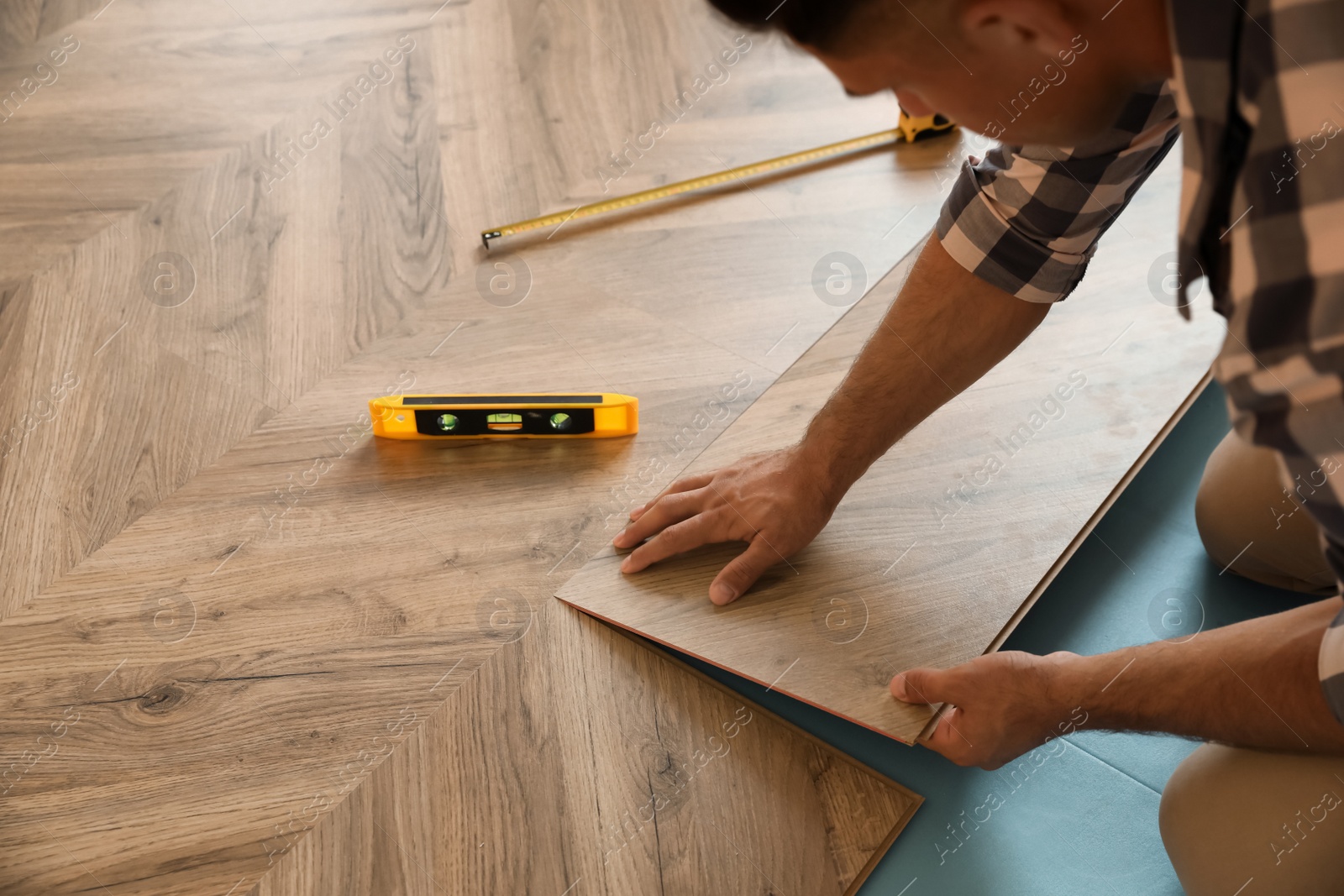 Photo of Professional worker installing new parquet flooring indoors, closeup