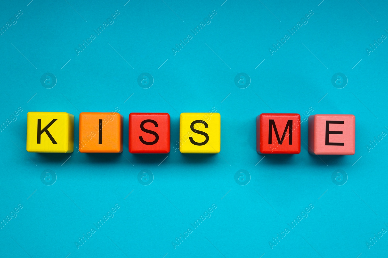 Photo of Colorful cubes with phrase Kiss Me on light blue background, flat lay