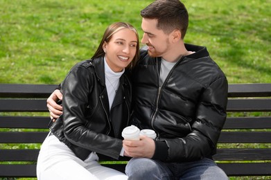 Photo of Lovely young couple with cups of coffee on bench outdoors. Romantic date