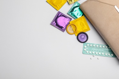 Photo of Flat lay composition with birth control pills and condoms on light background, space for text. Safe sex concept