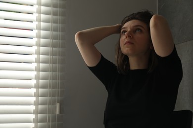 Photo of Sad young woman near closed blinds indoors, space for text