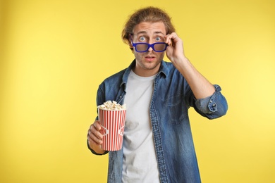 Emotional man with 3D glasses and popcorn during cinema show on color background