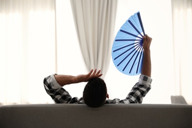 Photo of Man with hand fan on sofa. Summer season