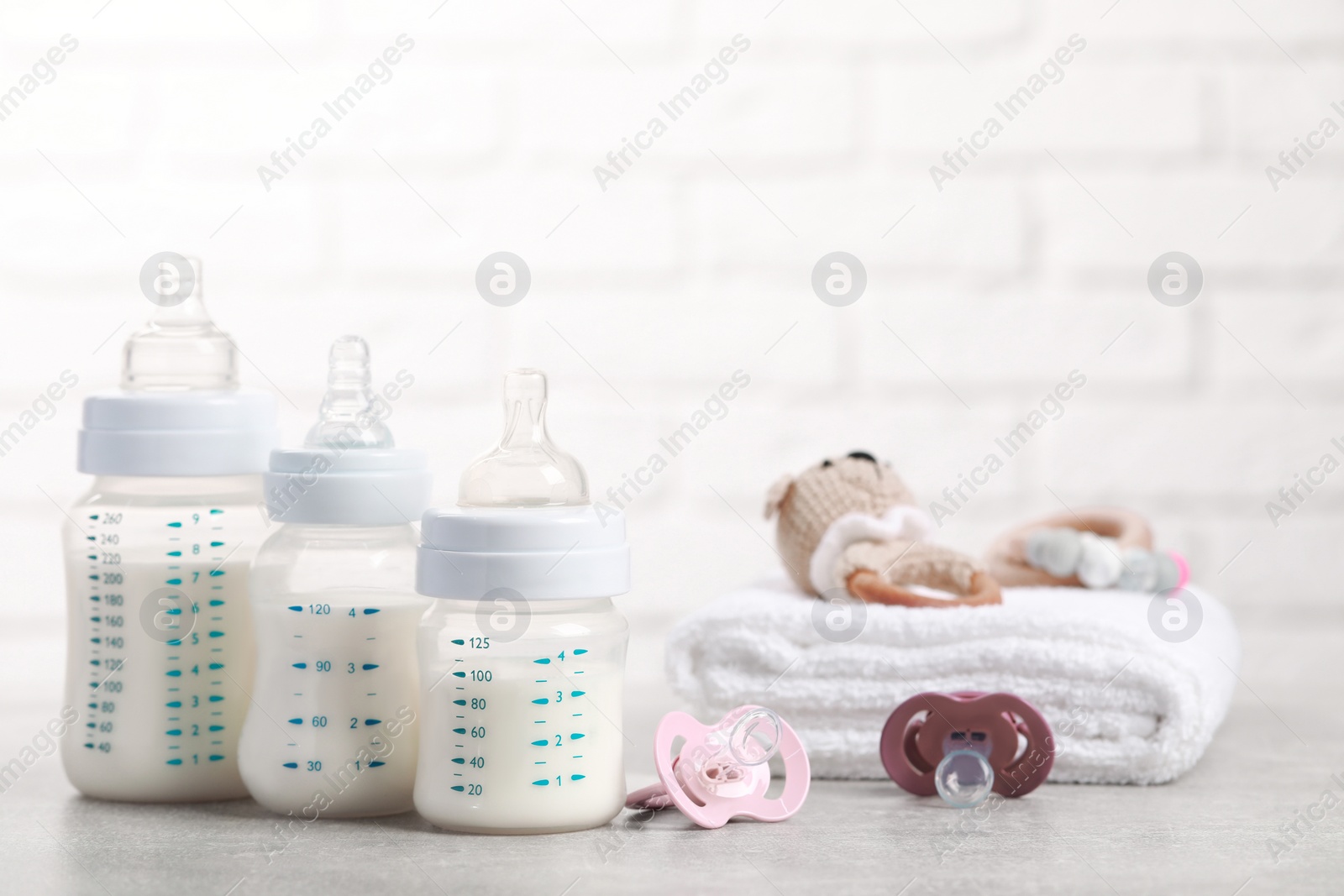 Photo of Feeding bottles with milk, pacifiers, toys and towel on light grey table