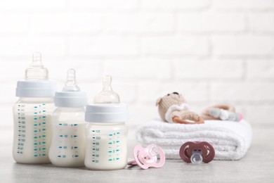 Feeding bottles with milk, pacifiers, toys and towel on light grey table