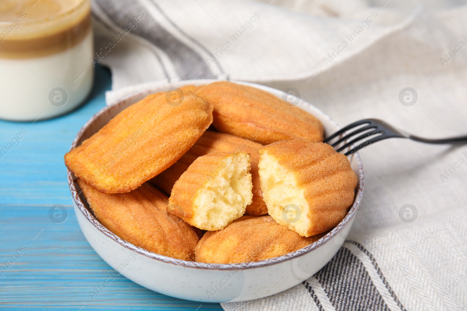 Photo of Tasty madeleine cookies in bowl on light blue wooden table