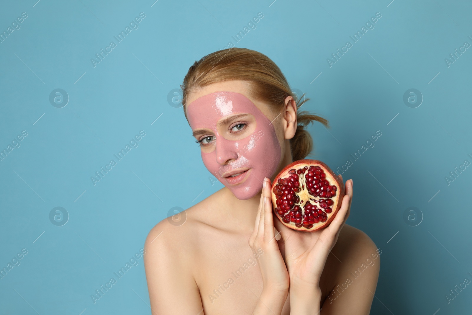 Photo of Young woman with pomegranate face mask and fresh fruit on light blue background