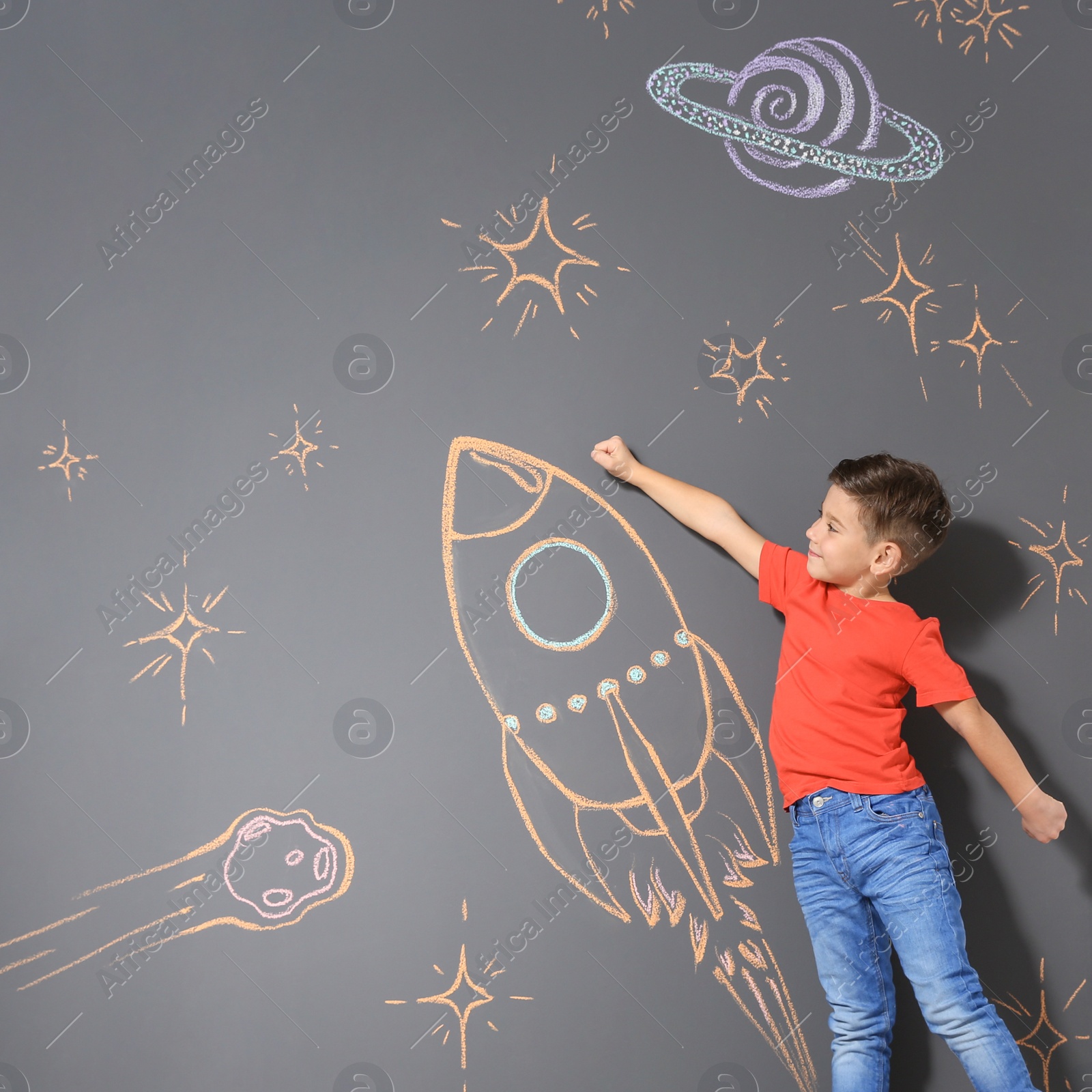 Photo of Cute little child playing with chalk rocket drawing on grey background