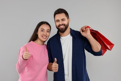 Photo of Happy couple with shopping bags showing thumbs up on grey background