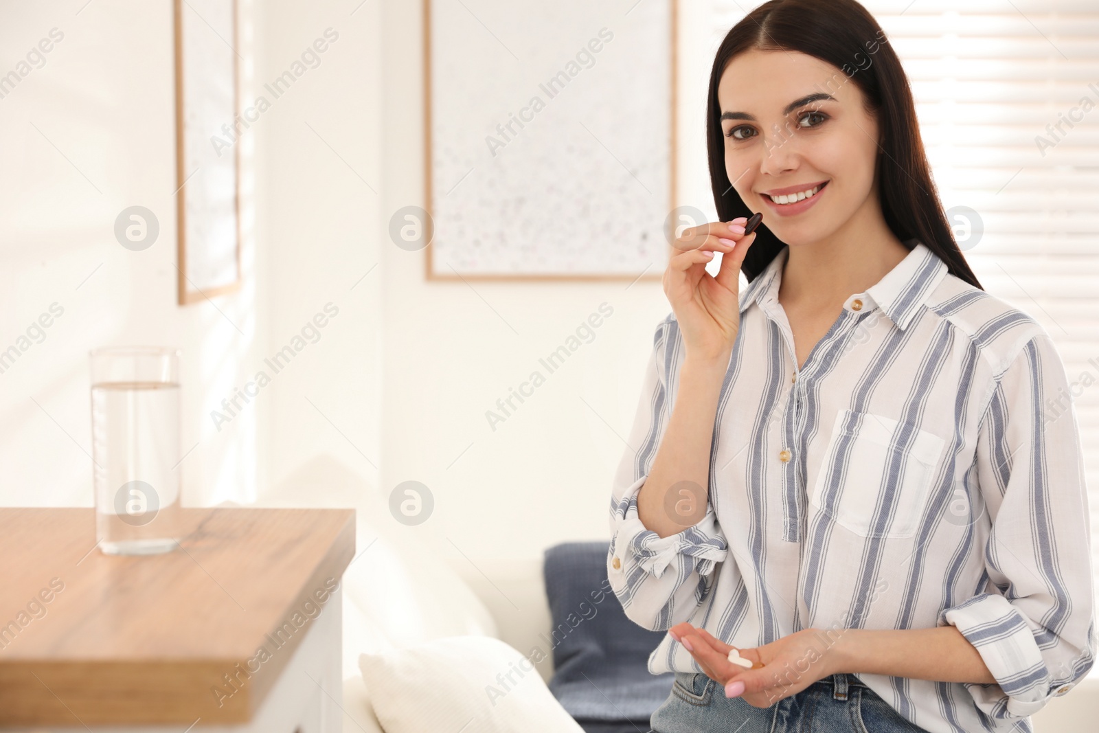 Photo of Young woman taking vitamins at home. Space for text