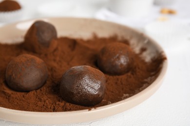 Photo of Plate with delicious chocolate truffles and cocoa powder on white table, closeup