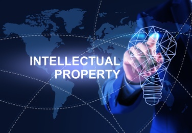 Image of Intellectual property concept. Man using virtual screen with world map and lamp bulb illustrations, closeup