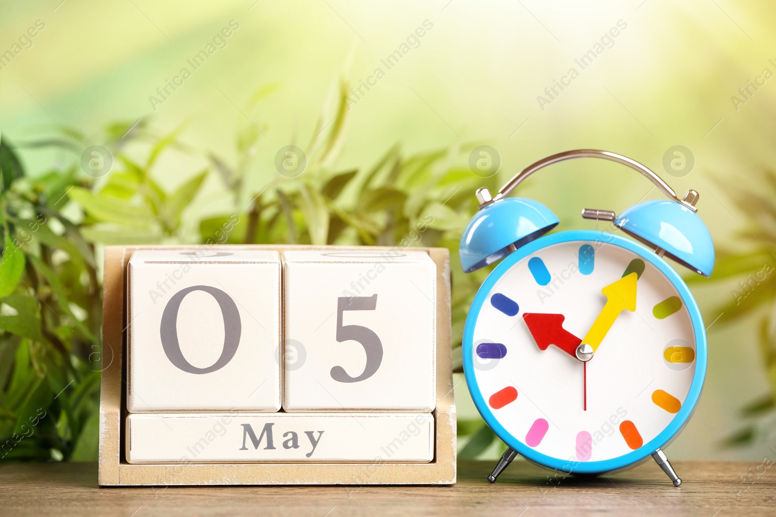 Image of Wooden block calendar and alarm clock on table against blurred green background
