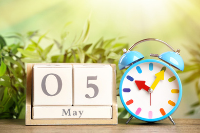 Wooden block calendar and alarm clock on table against blurred green background