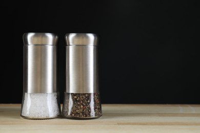Photo of Salt and pepper shakers on light wooden table against black background. Space for text