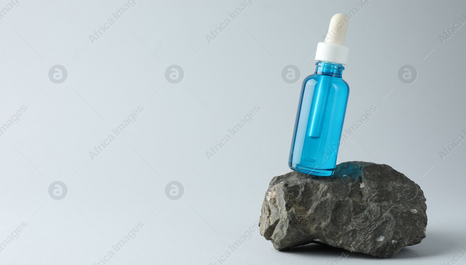Photo of Bottle of cosmetic serum on stone against light grey background, space for text