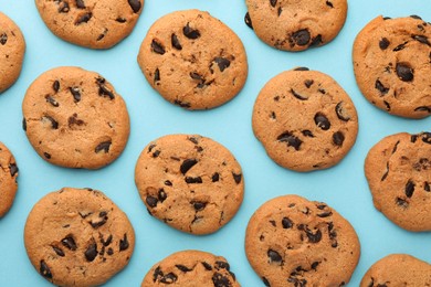 Many delicious chocolate chip cookies on light blue background, flat lay