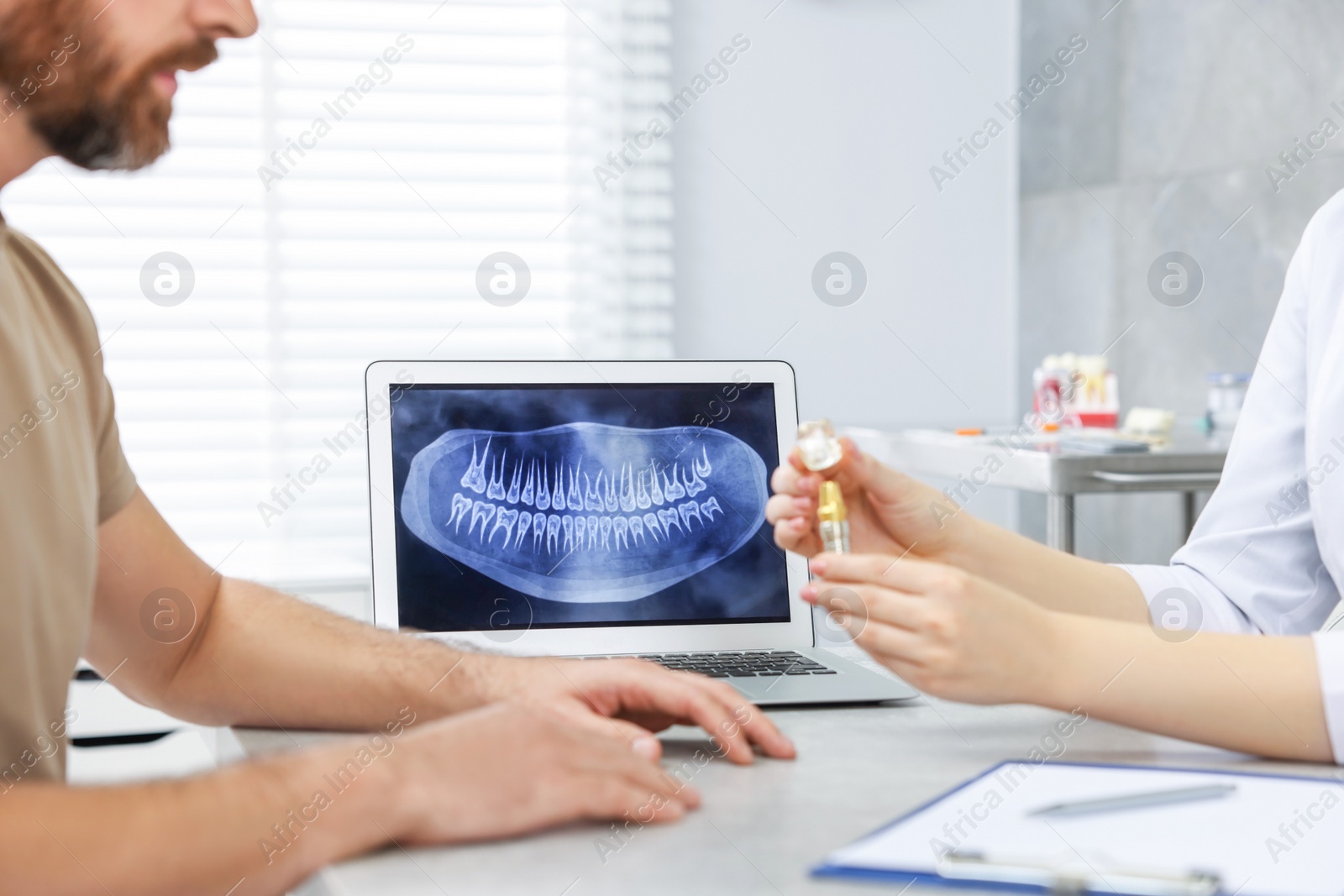 Photo of Doctor showing patient educational model of dental implant in clinic, closeup