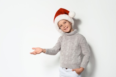 Photo of Cute little boy in warm sweater and Christmas hat on white background