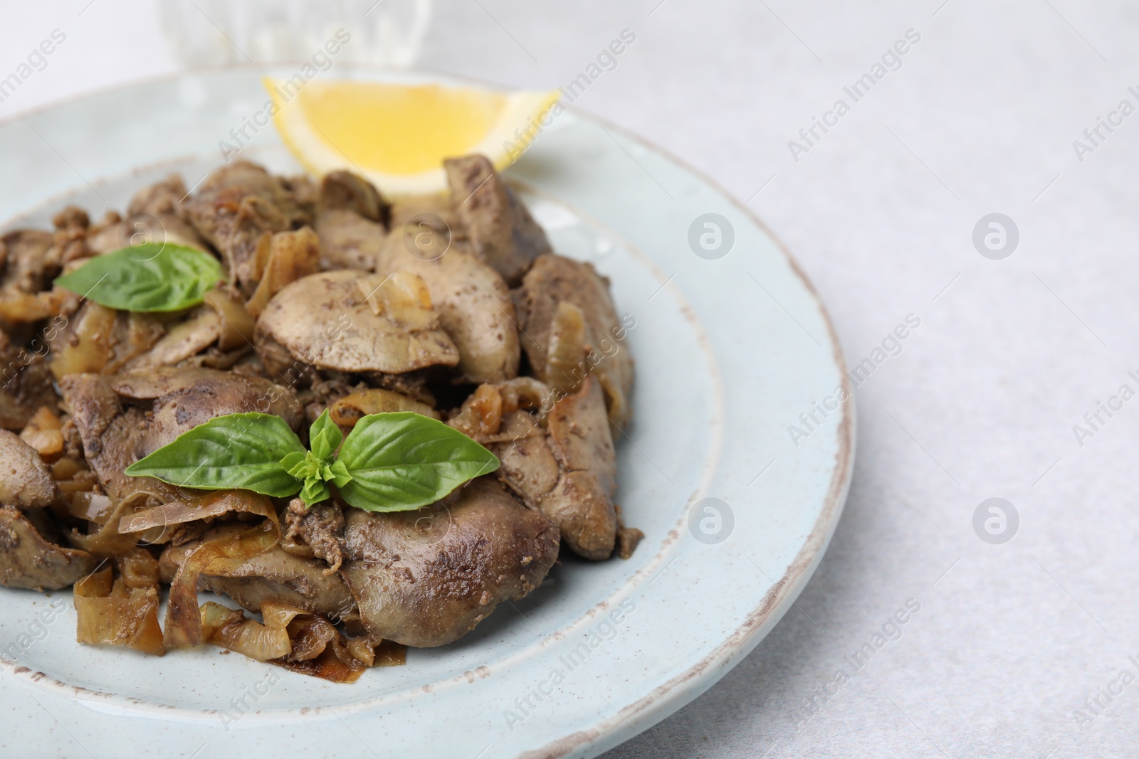 Photo of Delicious fried chicken liver with onion and basil on light table, closeup. Space for text