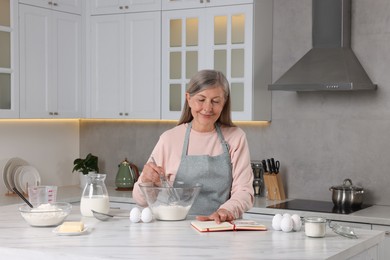 Senior woman with recipe book cooking in kitchen