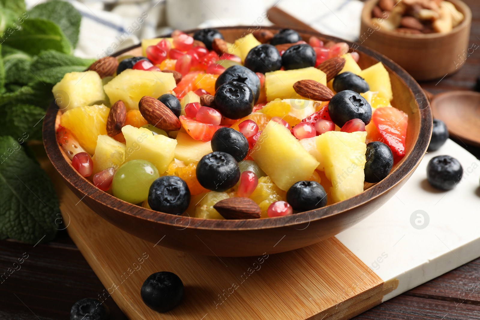 Photo of Delicious fruit salad in bowl, berries, nuts and fresh mint on wooden table