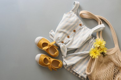 Stylish child clothes, shoes, flowers and mesh bag on grey background, flat lay. Space for text