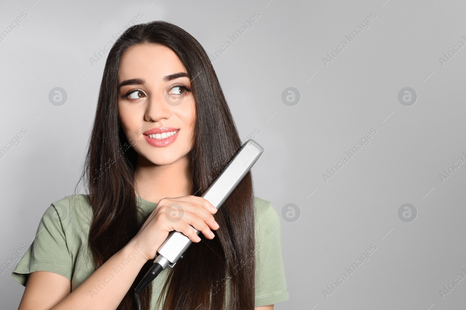 Photo of Happy woman using hair iron on grey background. Space for text