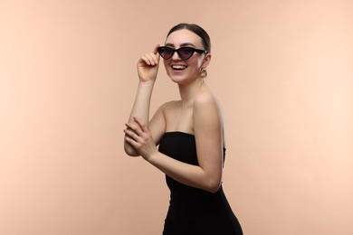 Photo of Portrait of beautiful young woman with sunglasses on beige background