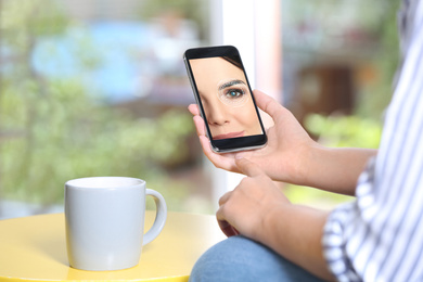 Image of Woman using smartphone with facial recognition system at table indoors, closeup. Biometric verification