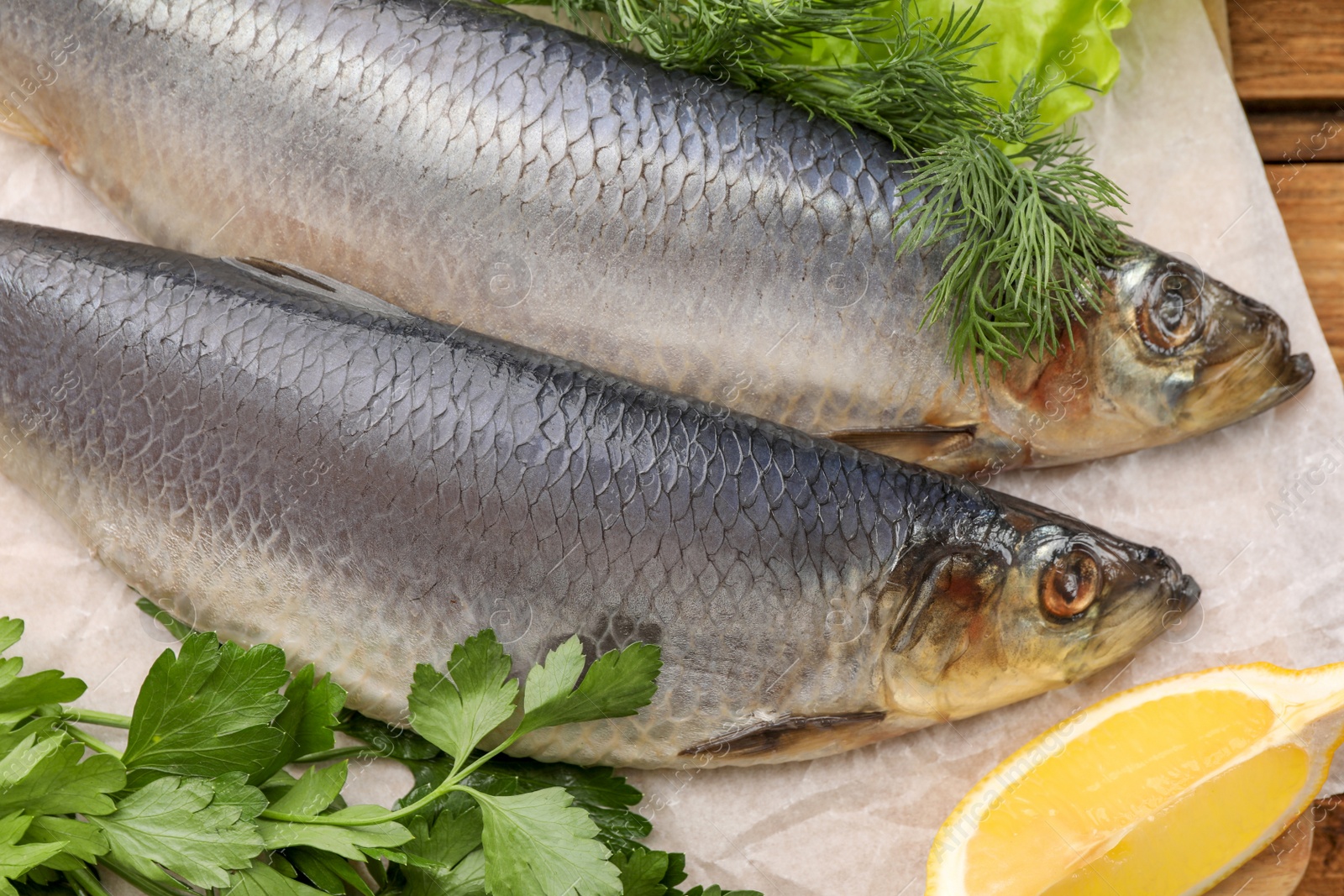 Photo of Board with delicious salted herrings, lemon and herbs on wooden table, closeup