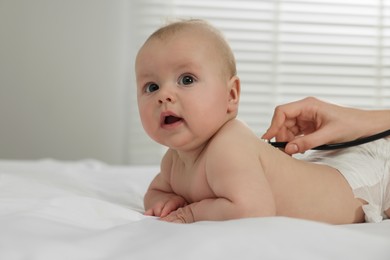 Photo of Pediatrician examining cute little baby with stethoscope in clinic, closeup