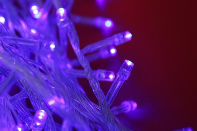 Glowing Christmas lights on dark red  background, closeup