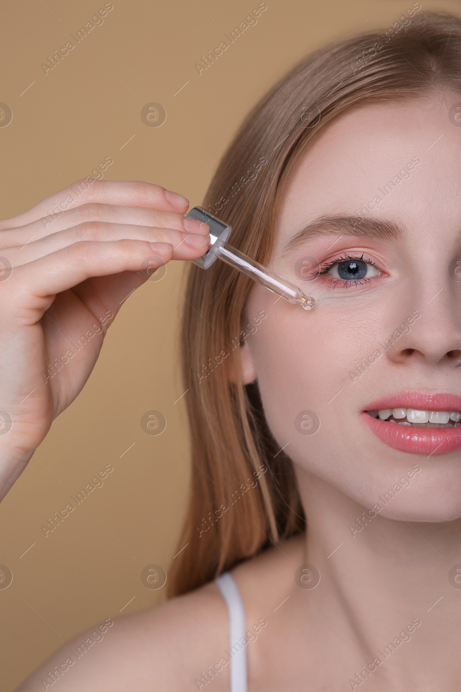 Photo of Woman applying essential oil onto face on light brown background, closeup