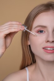 Woman applying essential oil onto face on light brown background, closeup