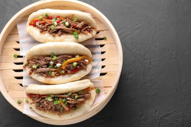 Photo of Delicious gua bao in bamboo steamer on black table, top view. Space for text