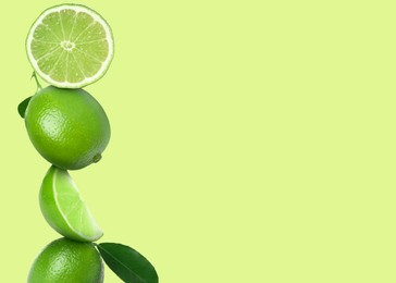 Image of Stacked whole and cut limes on yellowish green background, space for text