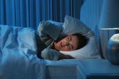 Photo of Unhappy young woman covering ears with pillow in bed at home. Noisy neighbours