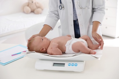 Photo of Doctor weighting cute baby in clinic, closeup. Health care