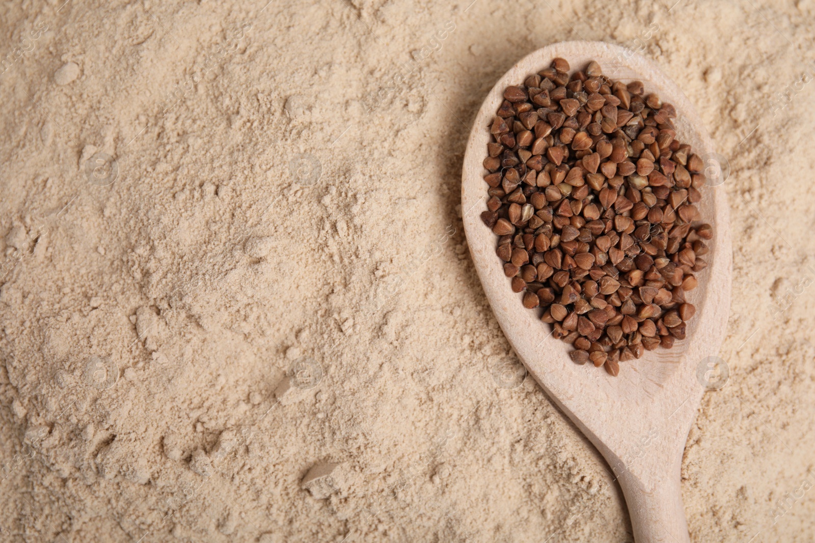 Photo of Spoon with buckwheat grains on flour, top view. Space for text