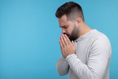 Photo of Sick man coughing on light blue background, space for text