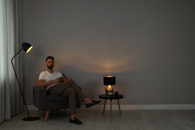 Man sitting in armchair with cup near gray wall, space for text