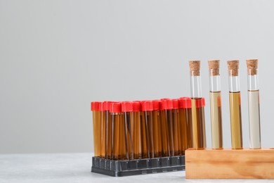 Photo of Test tubes with brown liquids in stands on white table against light background. Space for text