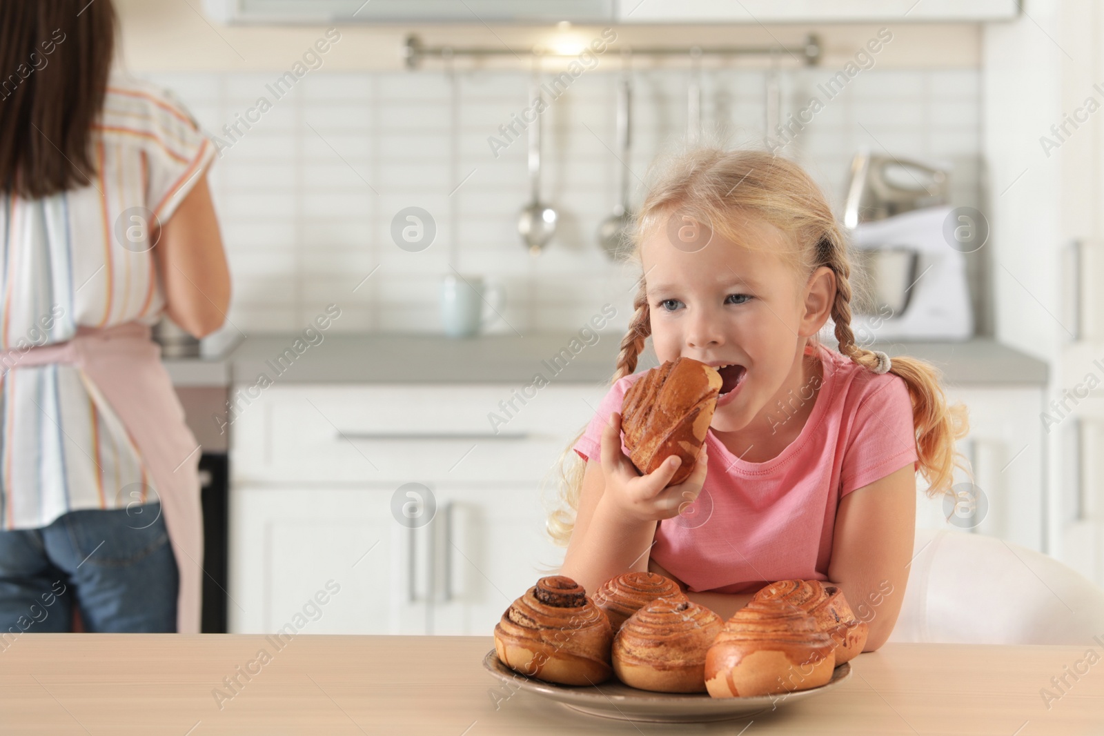 Photo of Little girl eating freshly oven baked buns in kitchen. Space for text