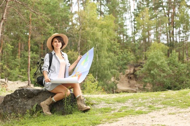 Photo of Young woman with map sitting on rock in forest. Camping season