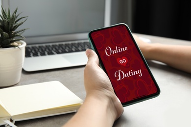 Woman visiting dating site via smartphone at table, closeup