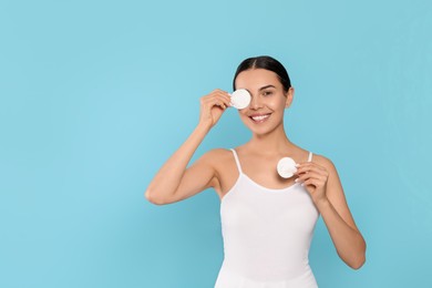 Young woman using cotton pads with micellar water on light blue background, space for text